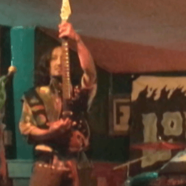 Algaenon holding his guitar straight up towards the ceiling.