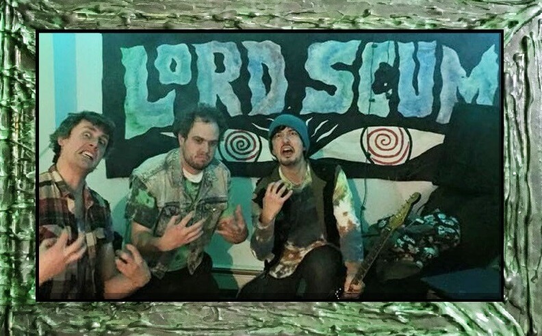 Three tie-dye-wearing weirdos pose with their hands open like claws towards themselves as they kneel for their really cool-looking band photo.